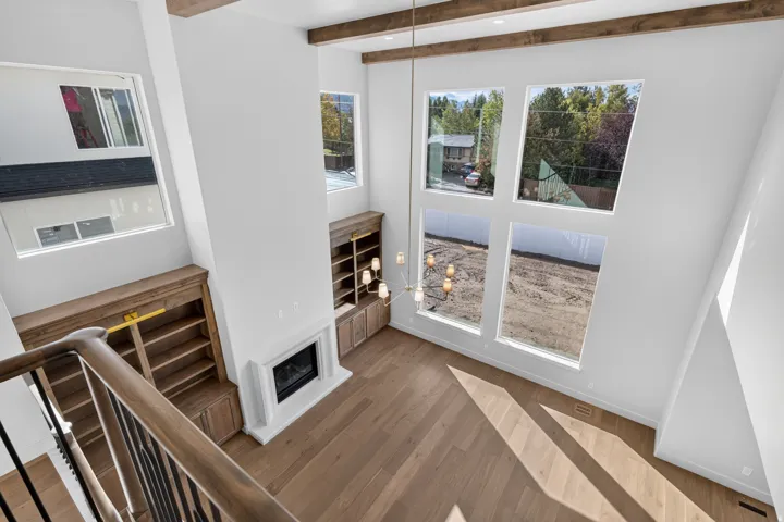 High ceilings featuring exposed wood beams, wood-finish flooring, a contemporary fireplace with mantel, built-in wooden shelving, and large windows