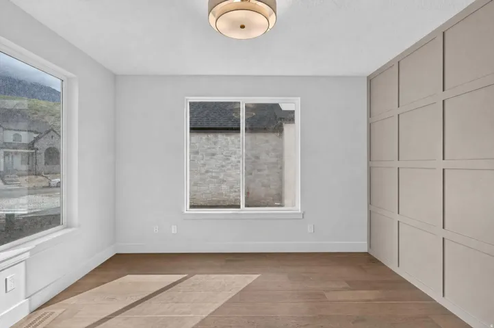 Wood-finish flooring, accent wall with panel molding, two large windows, and a flush mount ceiling light