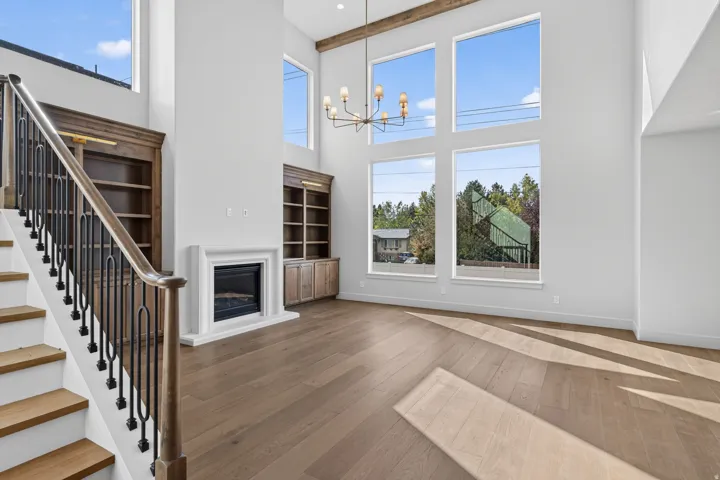 Wood-finish flooring, white fireplace with hearth, custom built-in cabinetry, two-story windows, and a decorative exposed beam