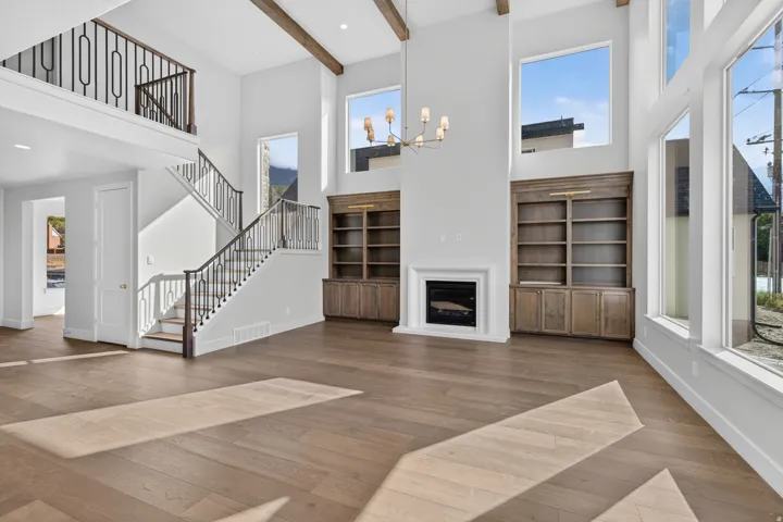 Vaulted ceiling featuring exposed wood beams, a built-in fireplace, custom built-in shelving, wood-finish flooring, and a contemporary chandelier