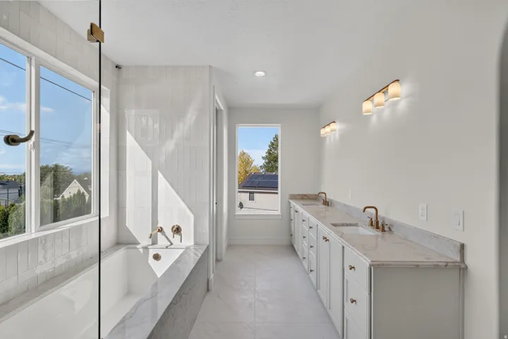 Double vanity with undermount sinks and brass-finish faucets, white shaker cabinetry, stone countertops, and recessed lighting