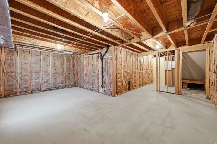 Unfinished basement space featuring a concrete floor, exposed wood framing, and ceiling joists