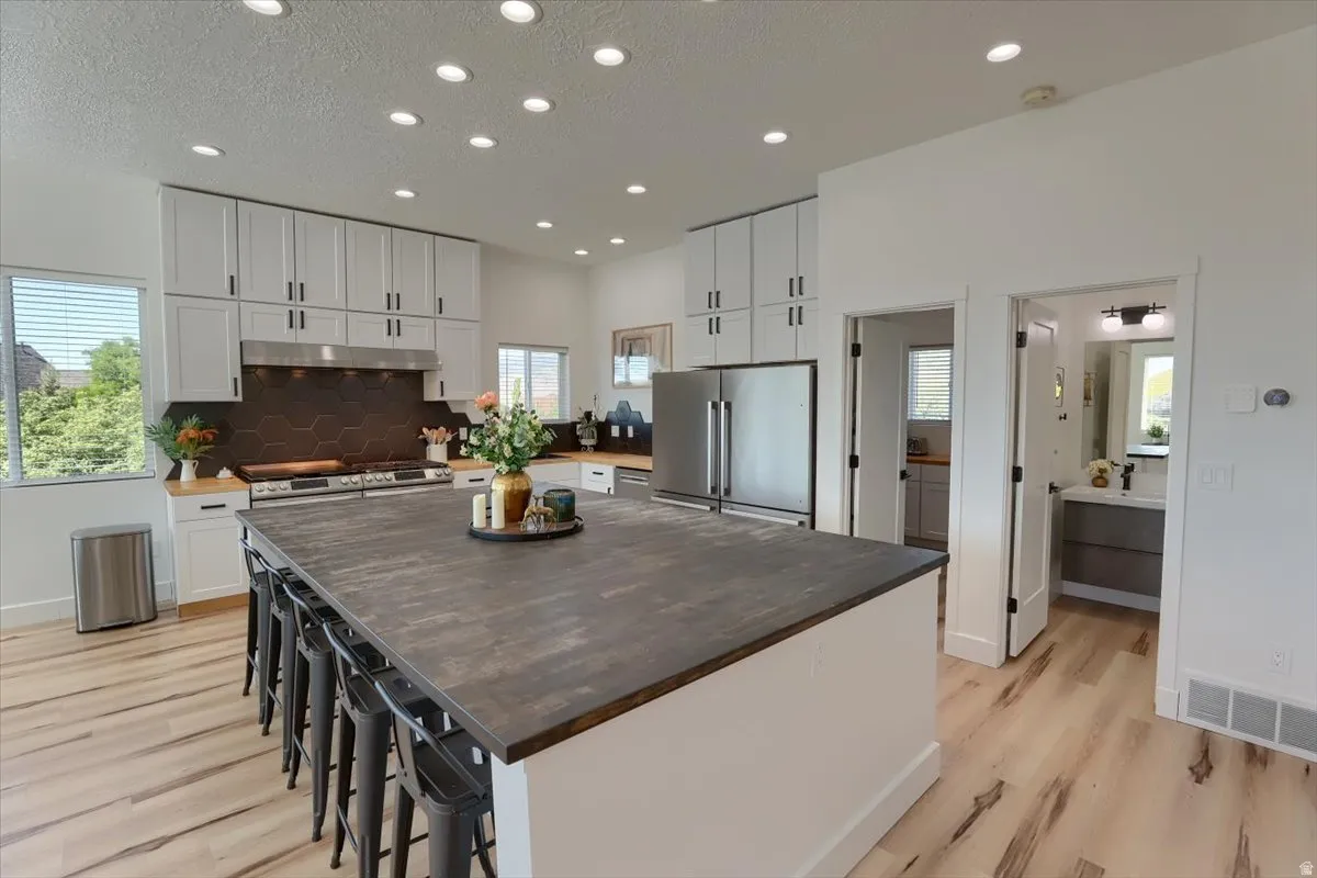 Open-concept kitchen featuring light-finish flooring, recessed lighting, white cabinetry with dark hardware, a center island with seating, and stainless steel appliances