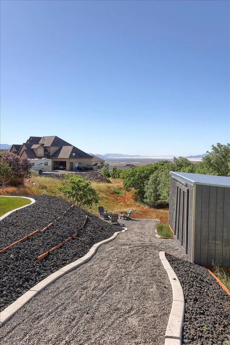 Terraced outdoor space featuring a graveled pathway, raised landscape beds with dark rock, and a dedicated patio area