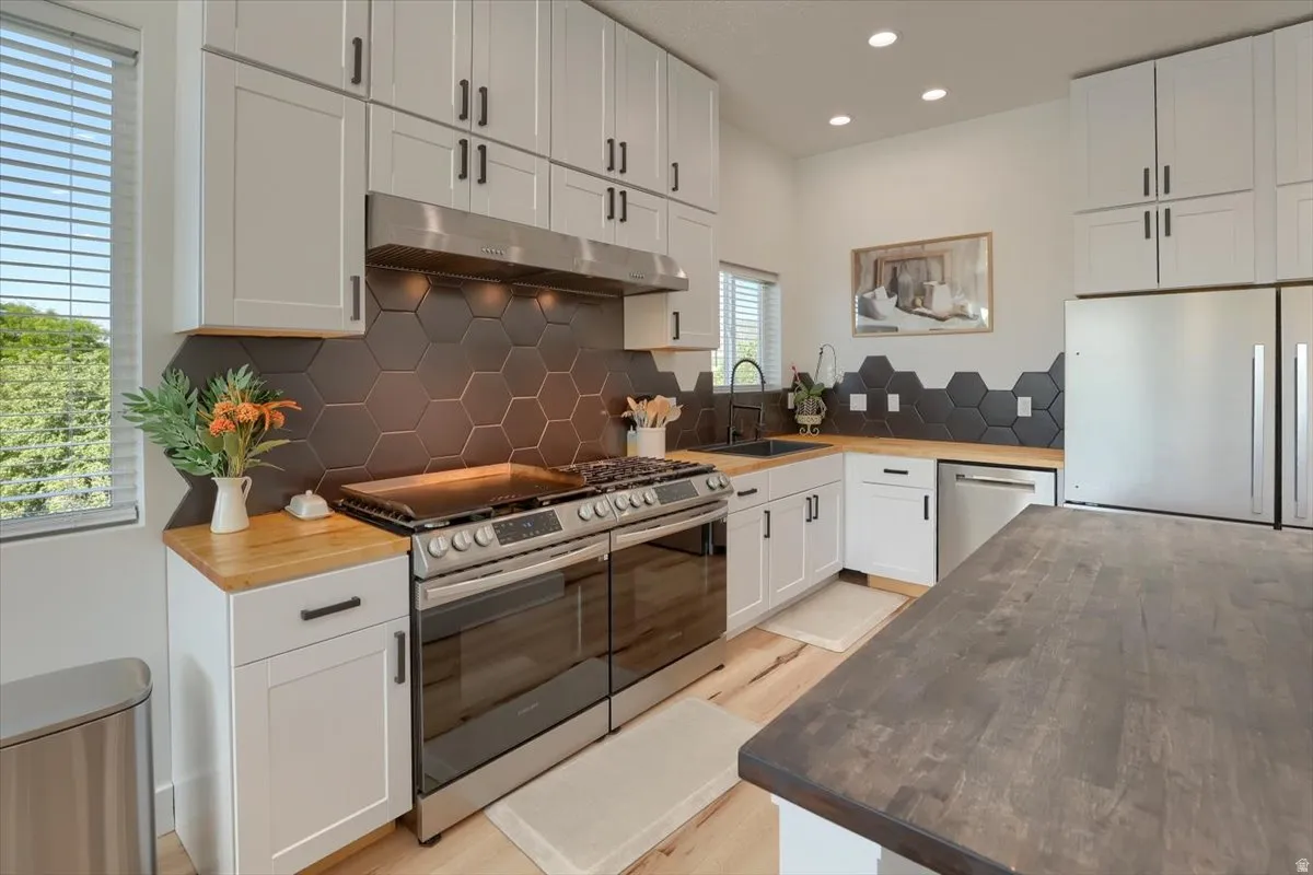 Modern kitchen featuring white shaker-style cabinetry with matte black hardware, hexagonal dark tile backsplash, wood-finish countertops, stainless steel appliances, and recessed lighting