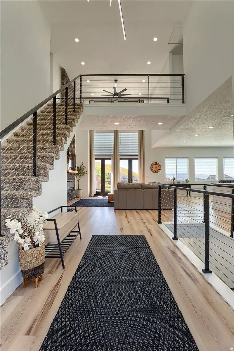 Expansive foyer featuring light wood-finish flooring, a carpeted staircase with contemporary cable railing, and recessed lighting
