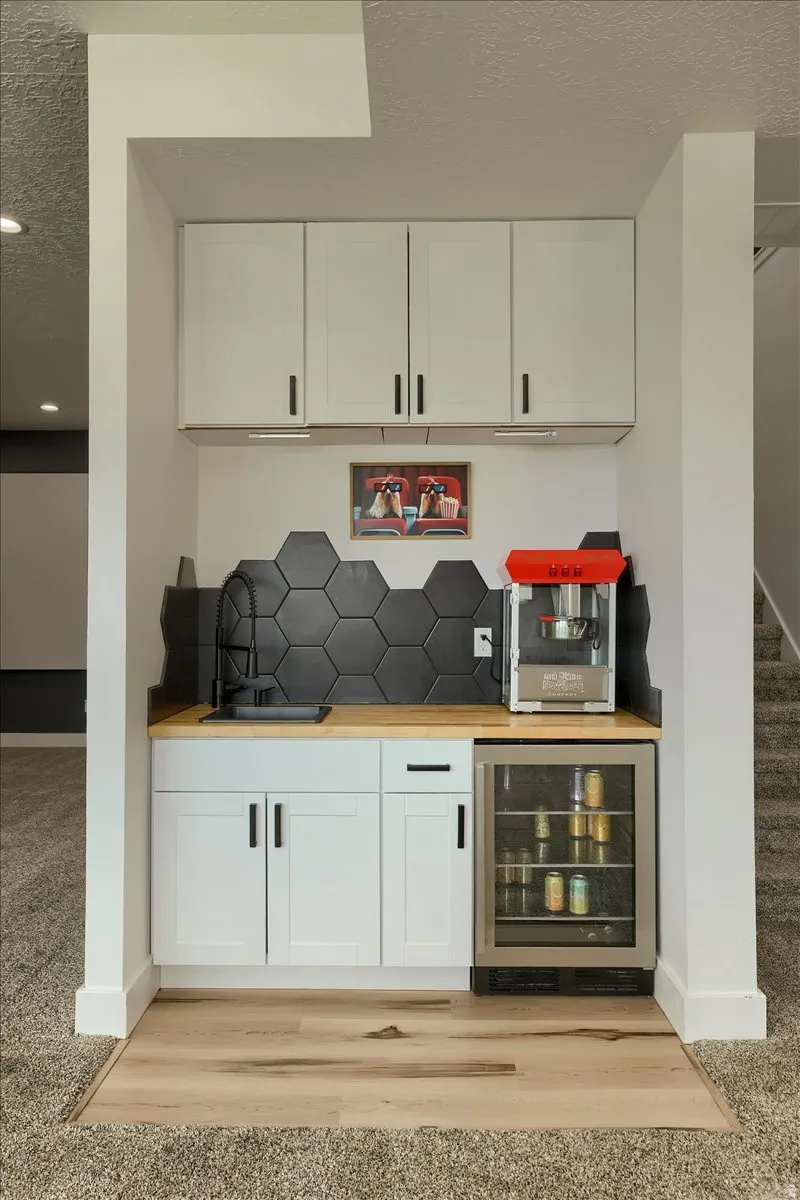 Built-in wet bar featuring white shaker-style cabinetry, a light wood-finish countertop, and a black hexagonal tile backsplash