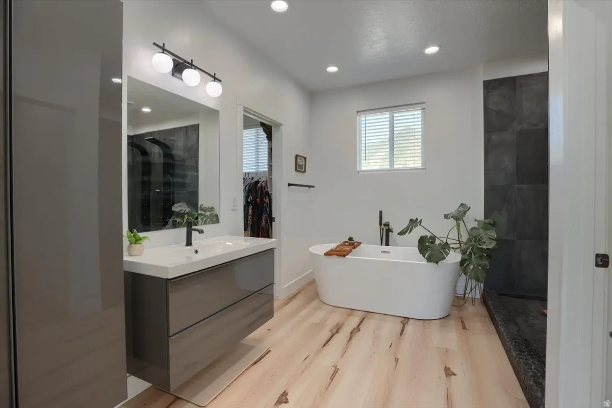 Bright bathroom featuring a floating vanity with integrated sink, contemporary black fixtures, light wood-finish flooring, a freestanding soaking tub, and large format dark tile in the shower