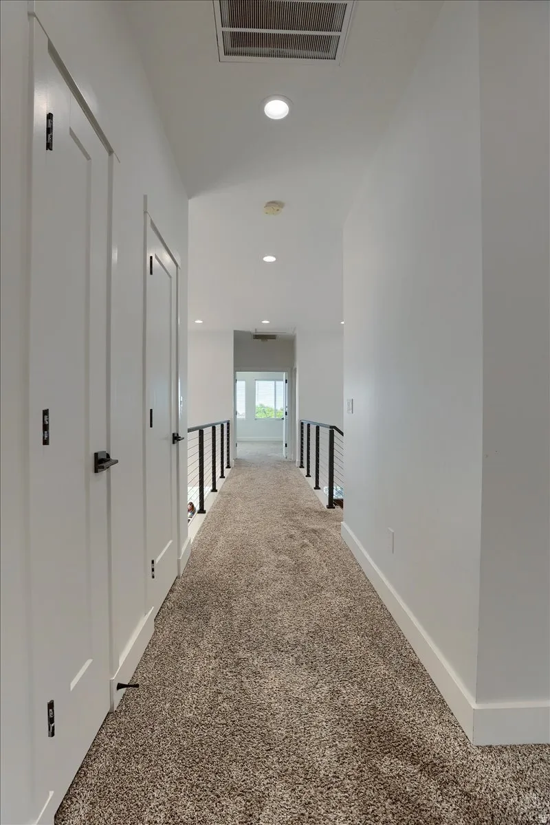 Contemporary hallway featuring carpet flooring, crisp white walls, recessed lighting, and modern black railings