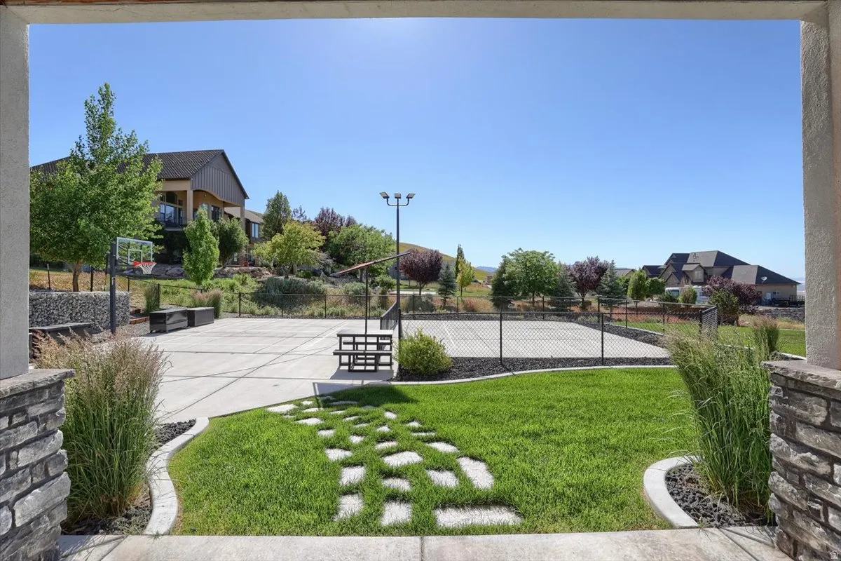 Expansive backyard featuring a manicured lawn, a concrete sport court with basketball hoop, and a fenced tennis court
