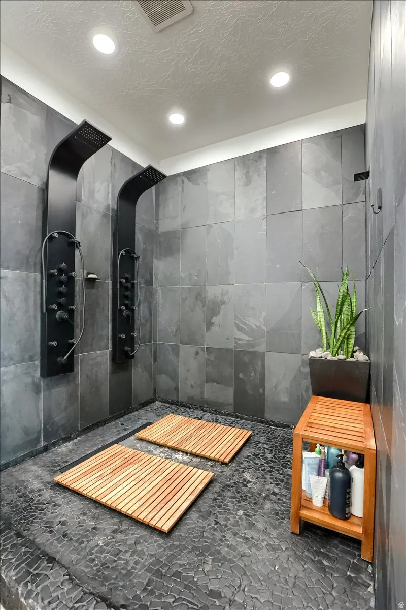 Spacious walk-in shower featuring dual matte black shower panels, pebble stone flooring, and large format wall tiling