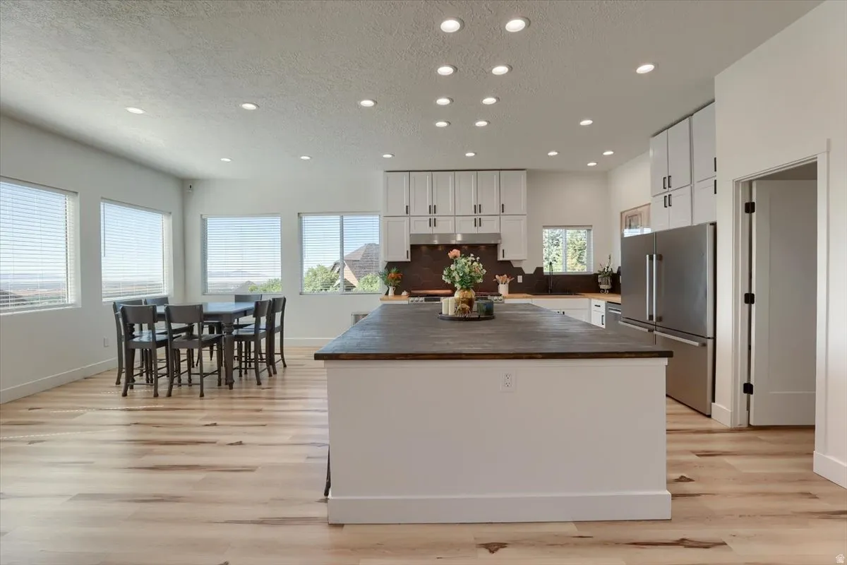 Spacious kitchen featuring a large central island with a wood-finish countertop, white cabinetry, and stainless steel appliances