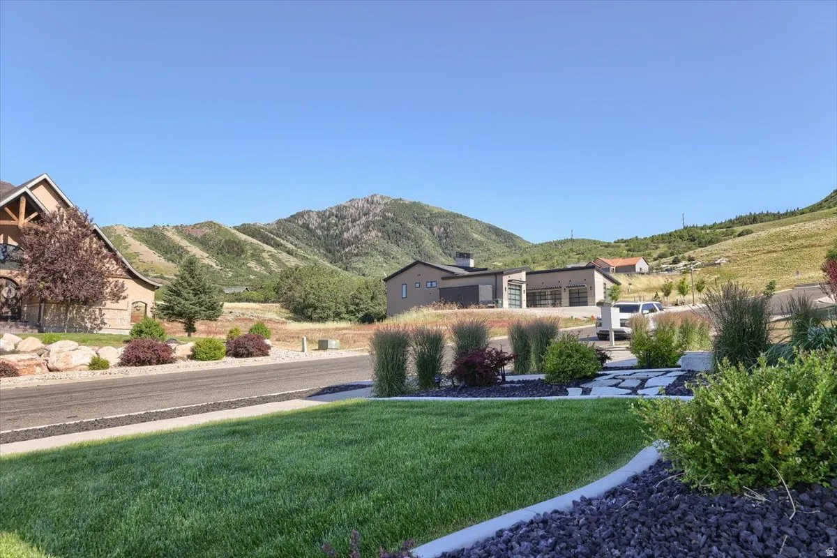 Expansive mountain backdrop with a manicured front lawn featuring decorative rock landscaping and mature plantings