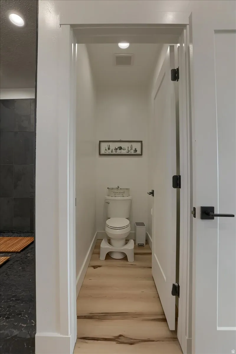 Private water closet featuring light wood-finish flooring, white baseboards, and a recessed ceiling light
