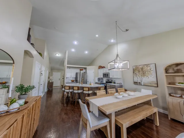 Open-concept living space featuring wood-finish flooring, vaulted ceilings, recessed lighting, and a modern kitchen with a large island and stainless steel appliances