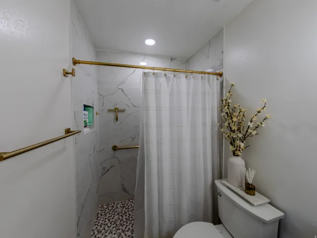 Shower stall featuring white marble-look tile walls, a mosaic pebble floor, and matte gold fixtures