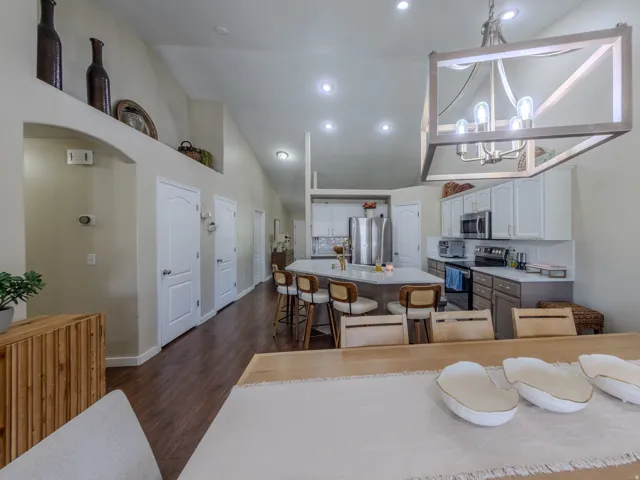 Open-concept kitchen and living area featuring high vaulted ceilings, recessed lighting, wood-finish flooring, a contemporary chandelier, and a kitchen island with seating