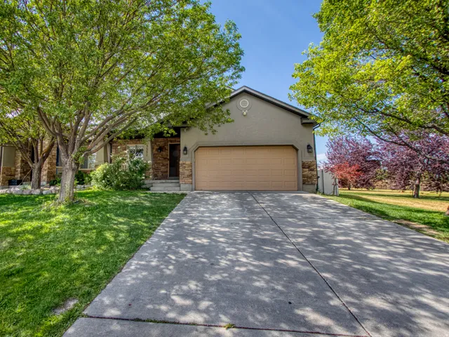 Front exterior featuring stone and stucco finishes, an attached garage, a concrete driveway, and mature landscaping