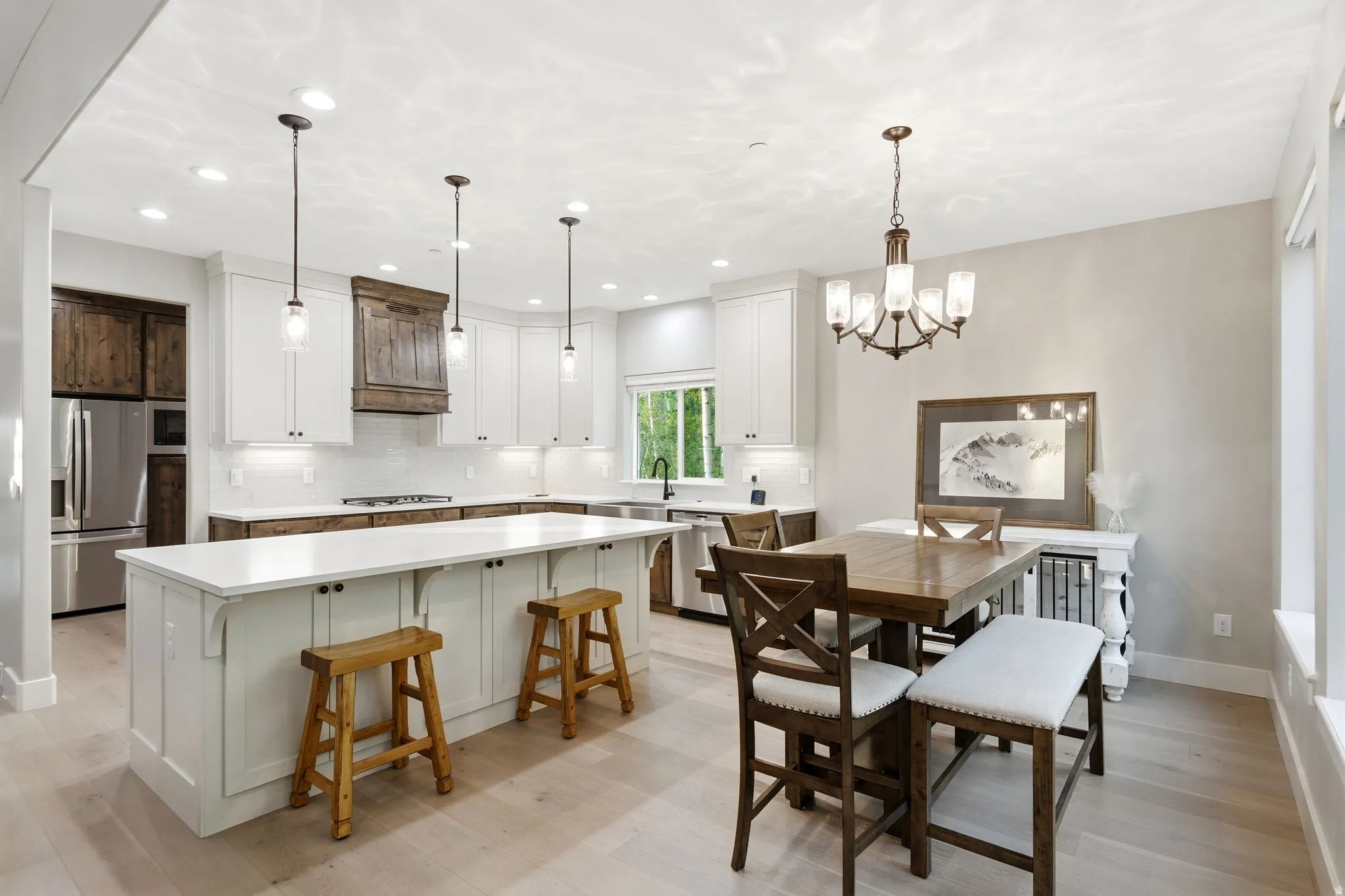 Contemporary kitchen featuring a large central island with pendant lighting, white cabinetry, dark wood-finish range hood, stainless steel appliances, and wood-finish flooring