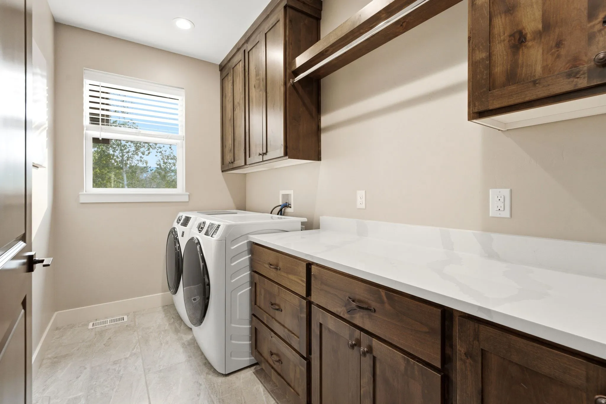 Laundry area featuring a window with blinds, wood-finish cabinetry, a white countertop, and tiled flooring