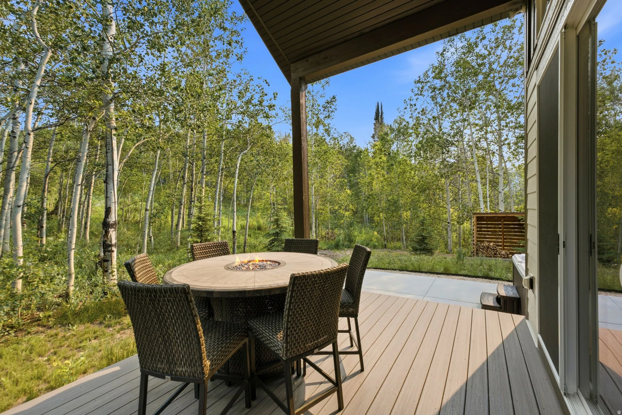 Covered outdoor deck with wood-finish composite decking, concrete patio, and mature aspen trees