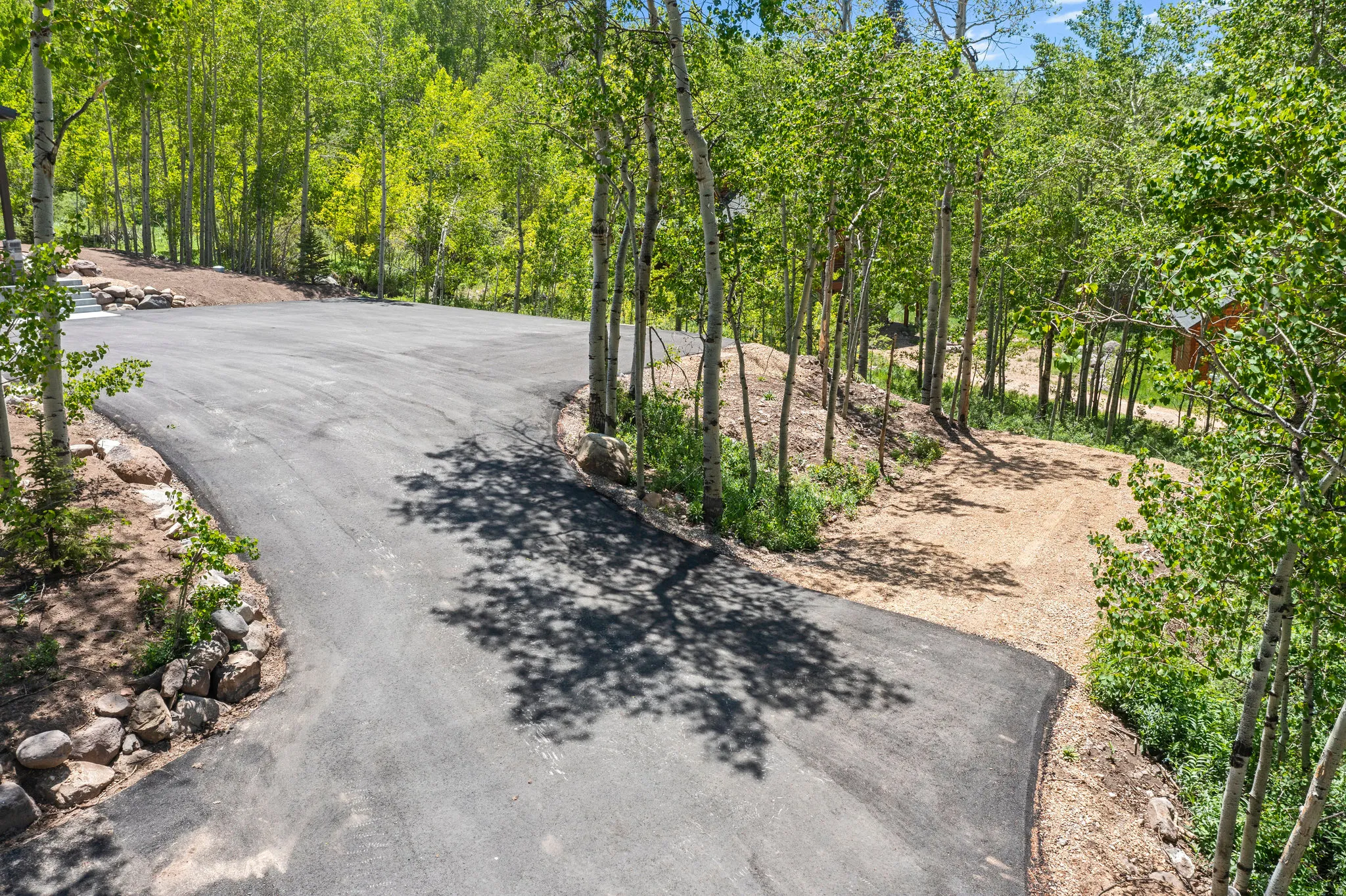 Paved driveway with a gravel turnaround bordered by mature trees