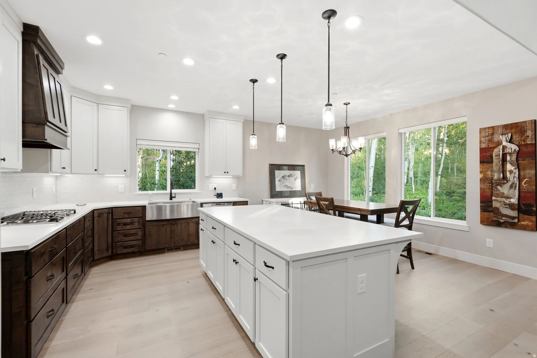 Gourmet kitchen featuring a large central island with white cabinetry, stainless steel farmhouse sink, white subway tile backsplash, and light wood-finish flooring