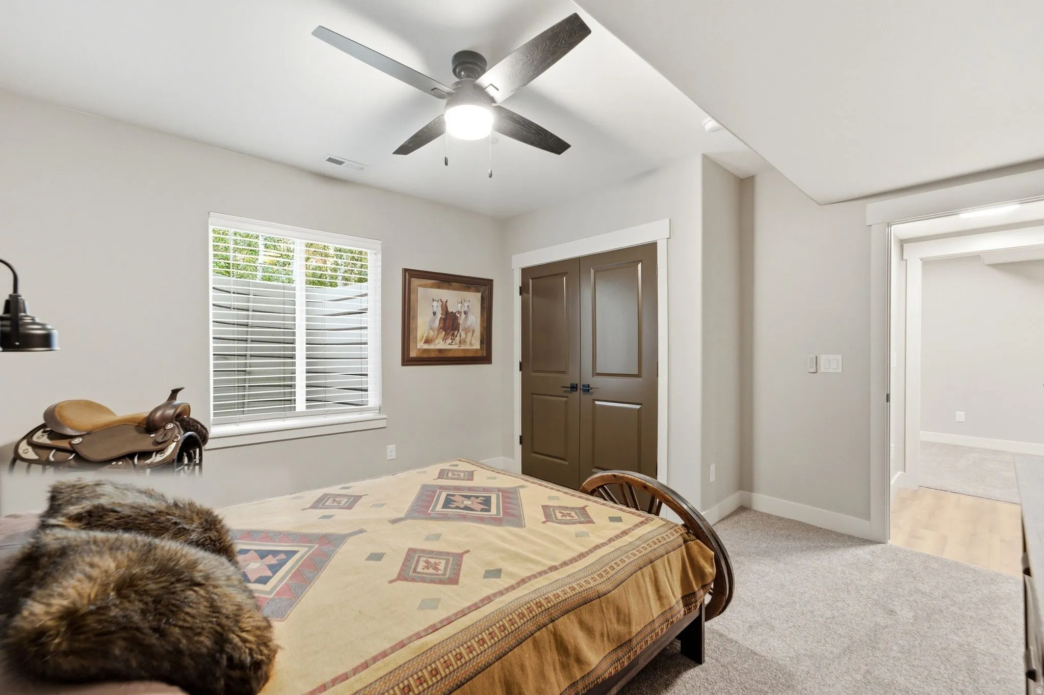 Carpeted room featuring a white-framed window with blinds, a ceiling fan with integrated lighting, and two-panel brown doors with black hardware