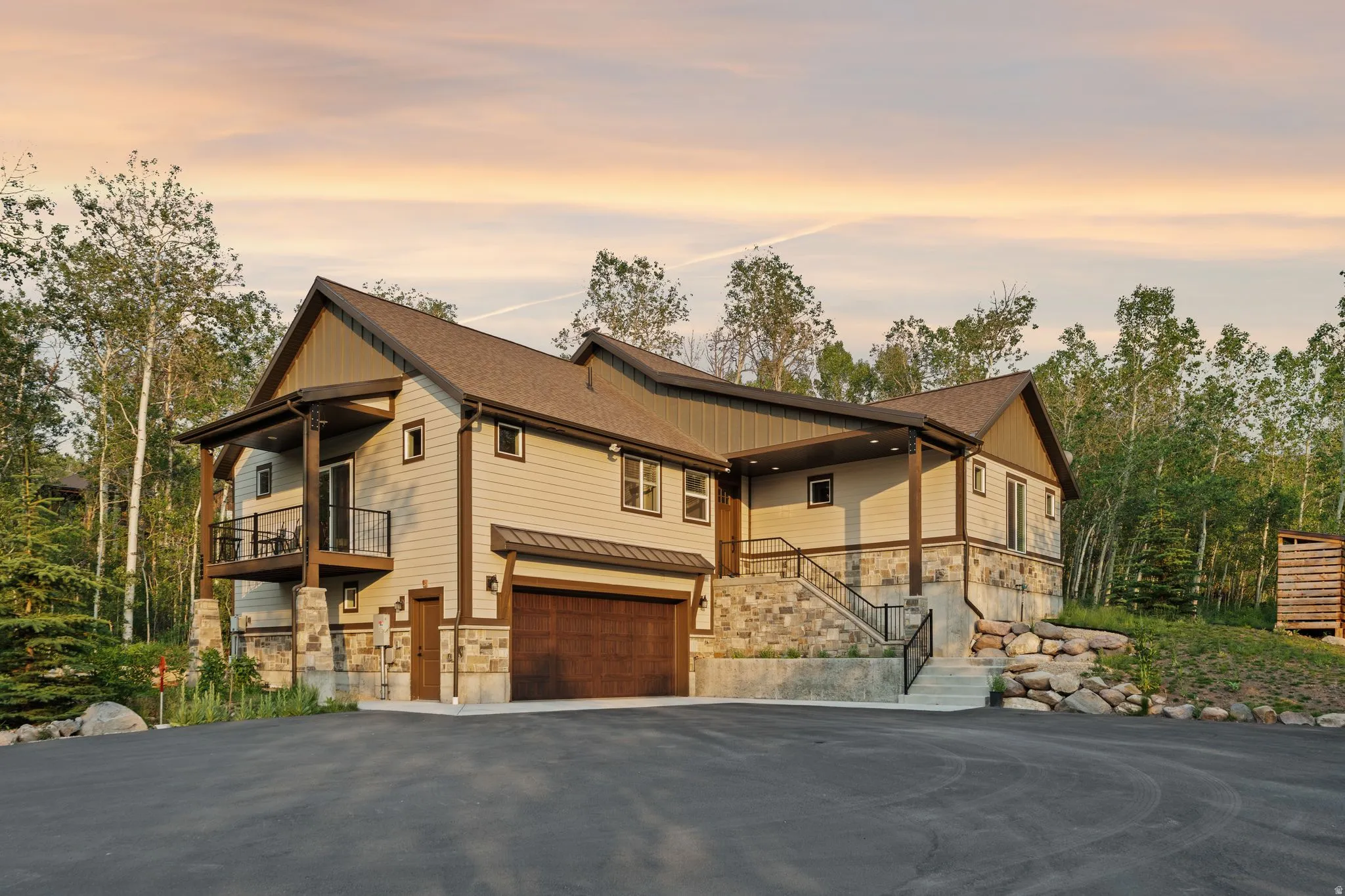 Contemporary multi-level residence featuring stone and siding facade, a two-car garage with a wood-finish door, and a covered balcony