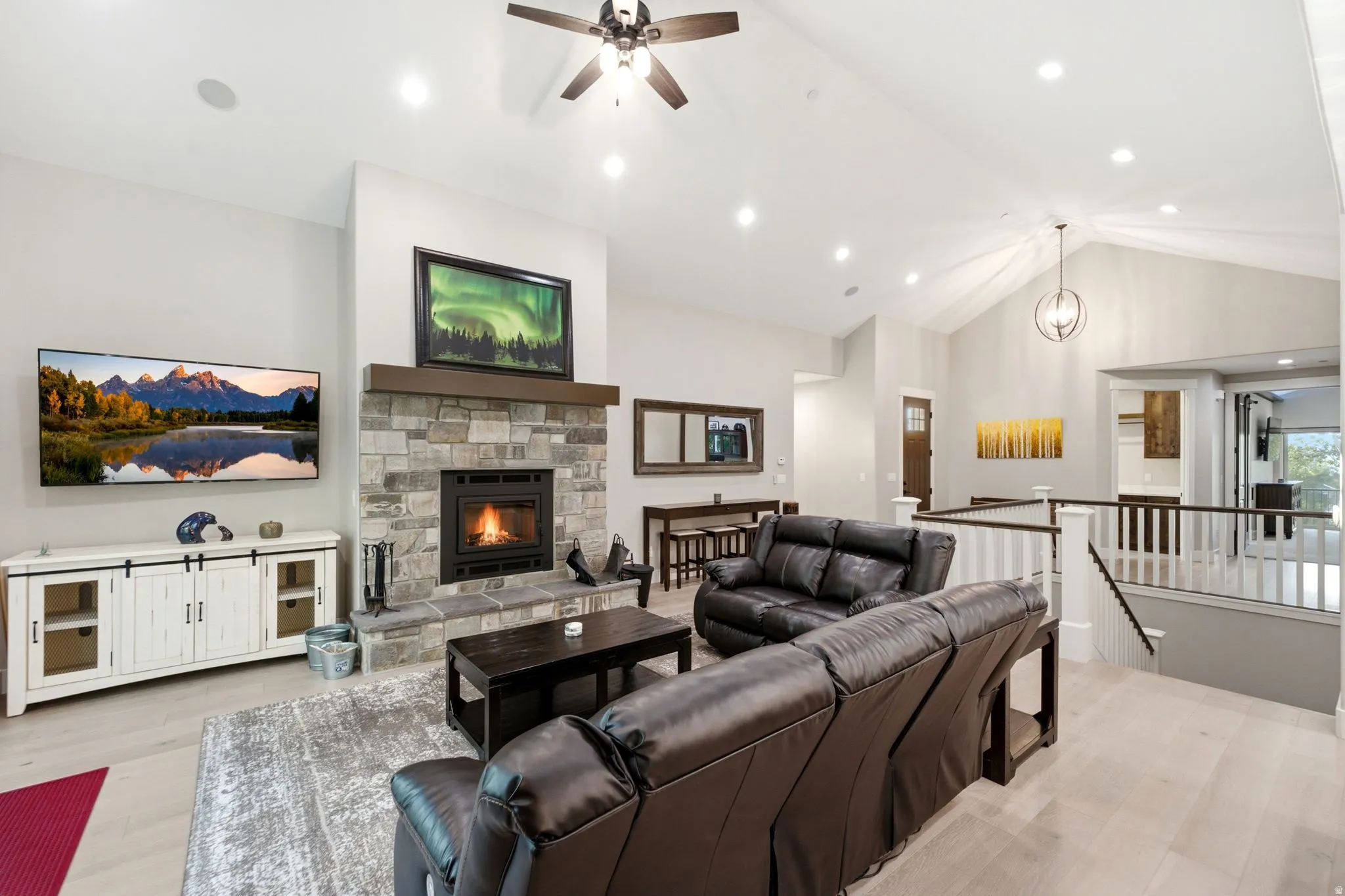 Spacious living area featuring a stone-clad fireplace with wood mantel, vaulted ceilings, recessed lighting, and light wood-finish flooring