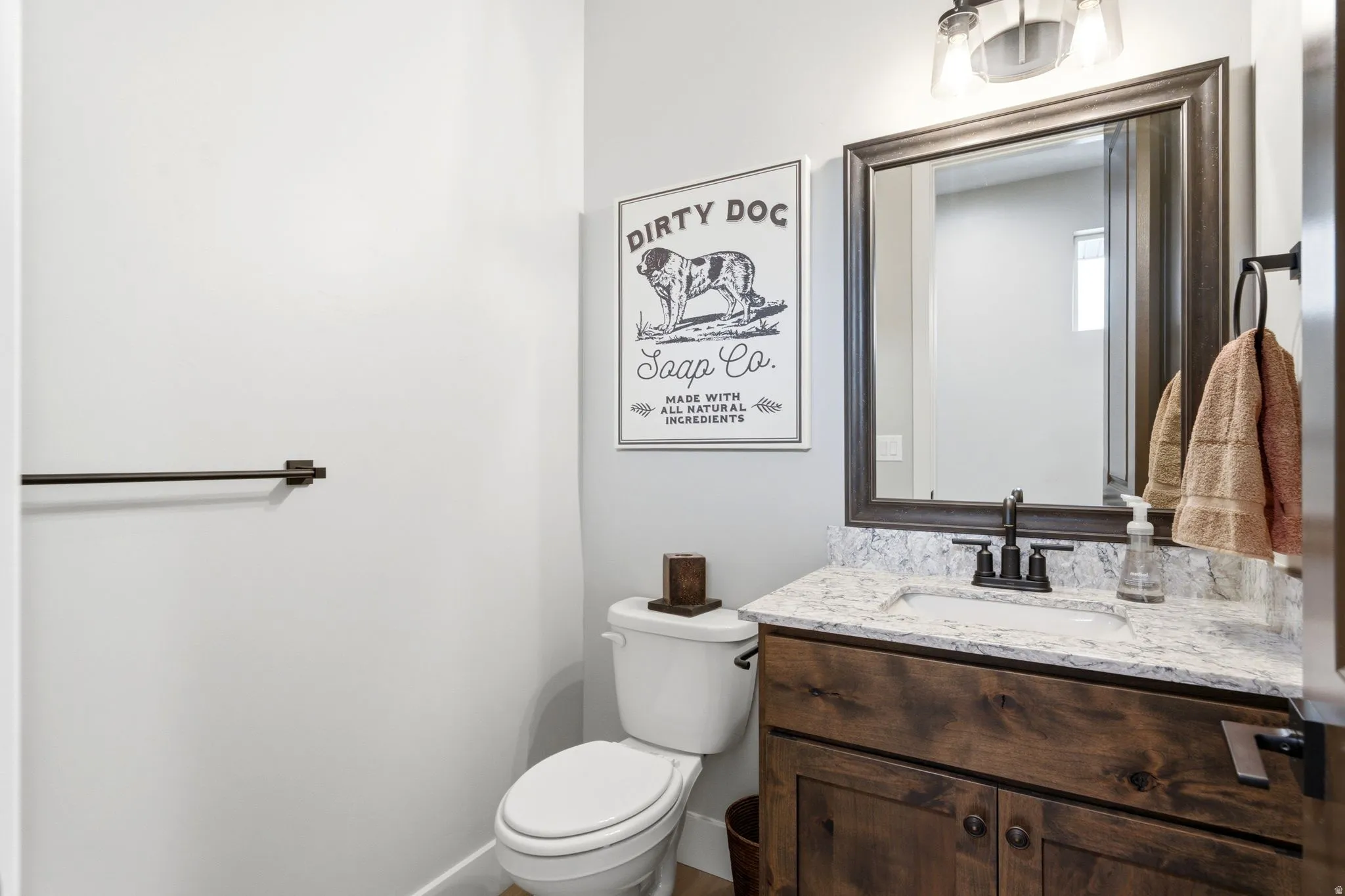 Powder room featuring a wood-finish vanity with a white countertop and undermount sink, framed mirror, and a wall-mounted light fixture