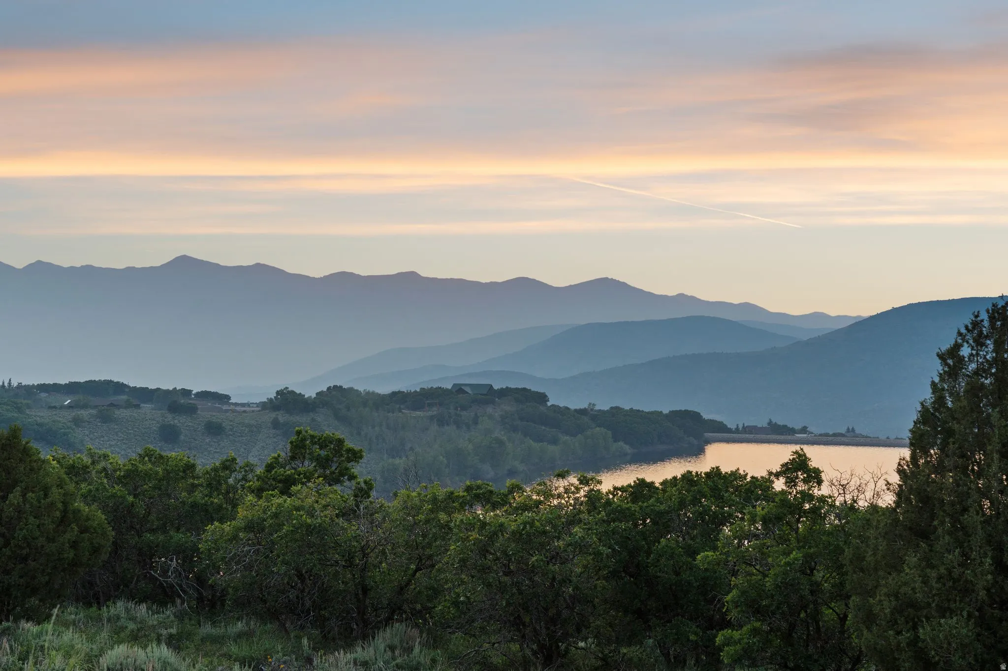 Expansive natural scenery featuring a prominent body of water, distant mountain ranges, and dense tree cover