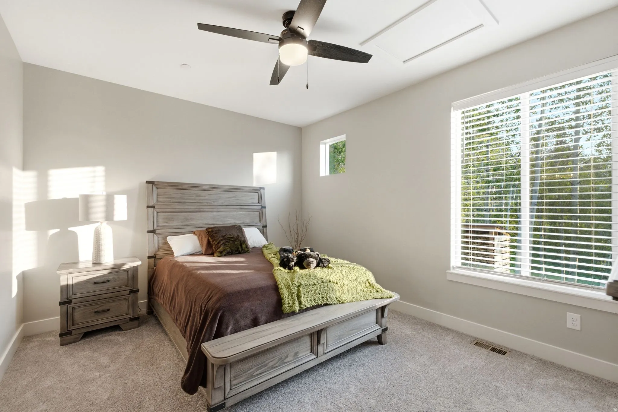 Carpeted room featuring a ceiling fan with integrated lighting, a large window with blinds, and an additional small square window