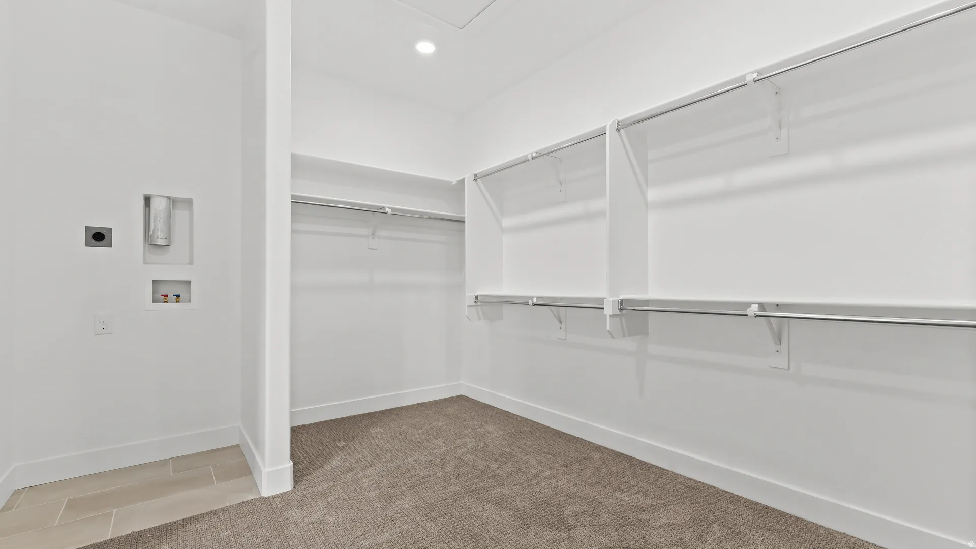 Dedicated laundry area with tile flooring and adjacent walk-in closet featuring built-in shelving, hanging rods, and carpet flooring