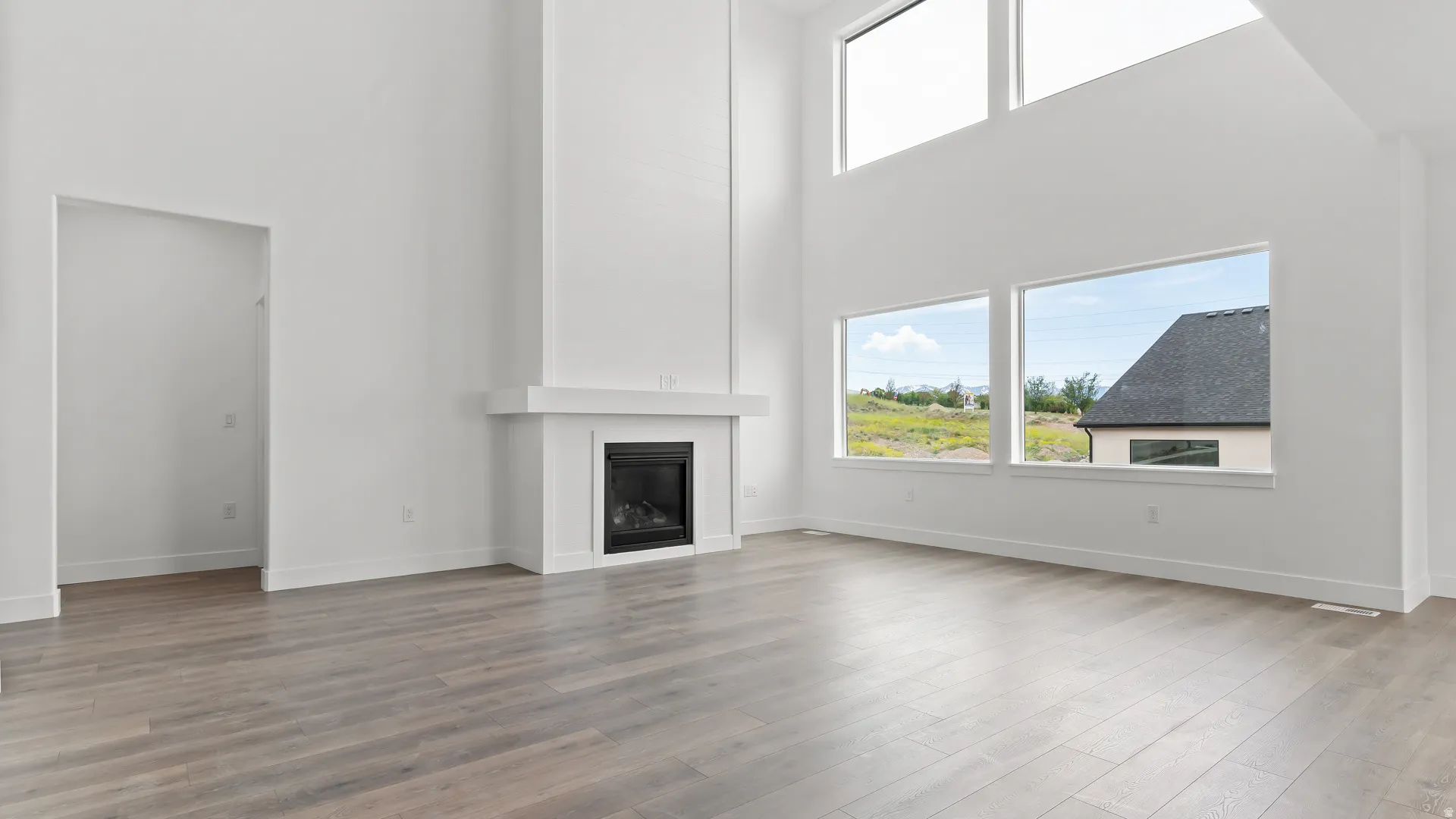 Spacious room with high ceilings, wood-finish flooring, a contemporary fireplace, and multiple large windows
