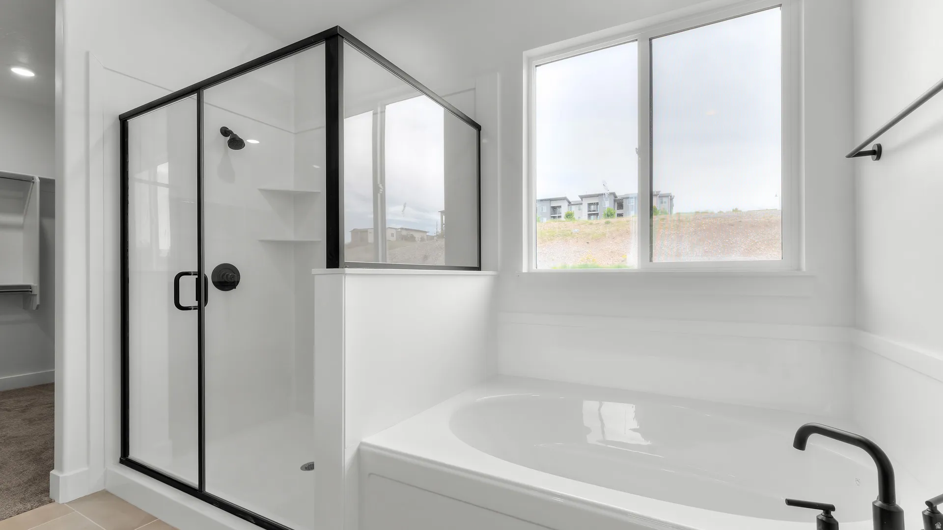 Modern bathroom featuring a soaking tub, glass-enclosed shower with matte black fixtures, and a large window