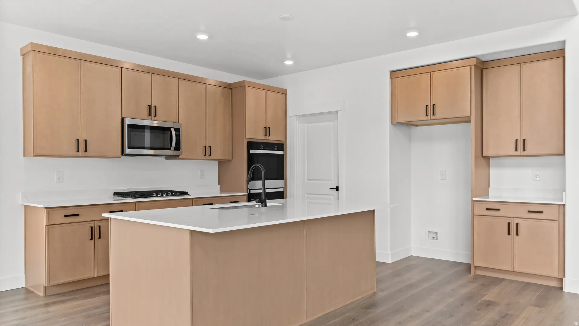 Modern kitchen featuring light wood-finish cabinetry, white countertops, and wood-finish flooring