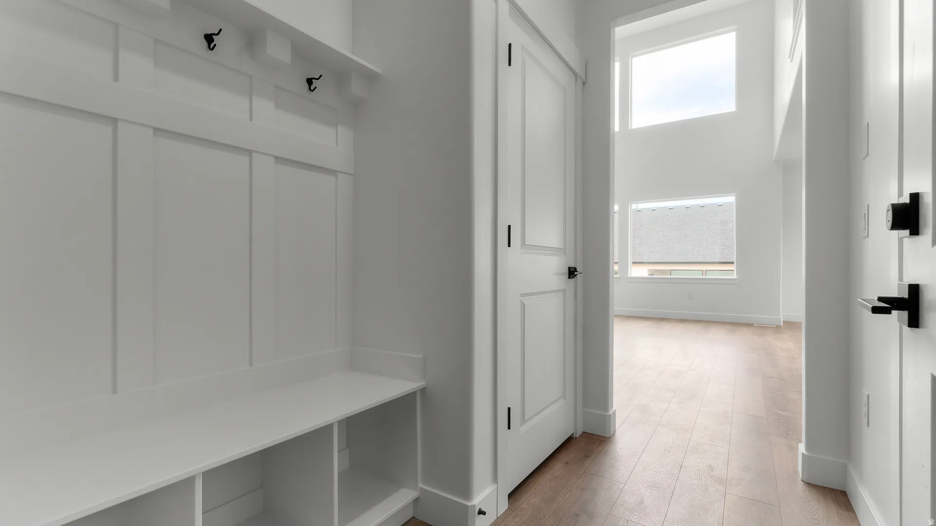 Entryway featuring a built-in bench with storage cubbies and coat hooks, wood-finish flooring, two-panel interior doors with matte black hardware, and double-height ceilings with expansive windows