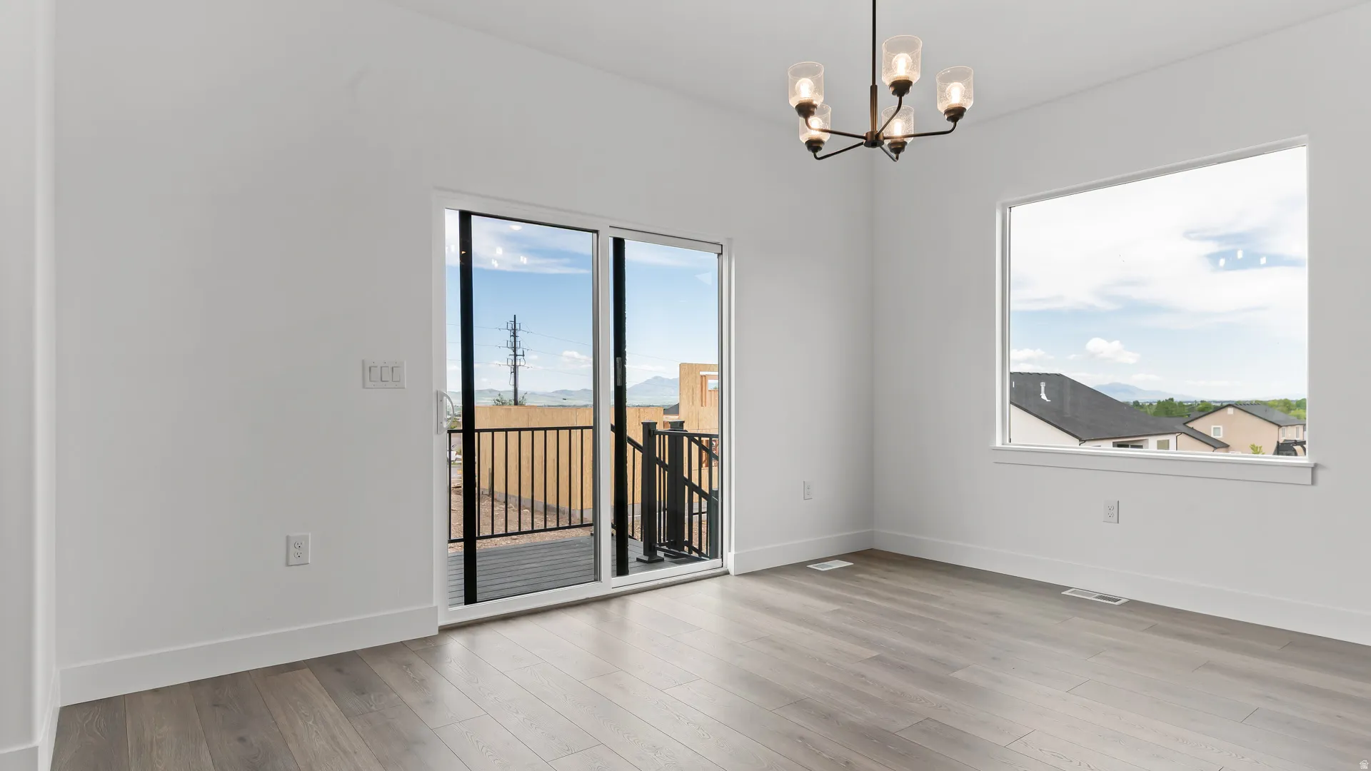 Spacious room featuring wood-finish flooring, a contemporary chandelier, large picture window, and direct access to an outdoor balcony with metal railings