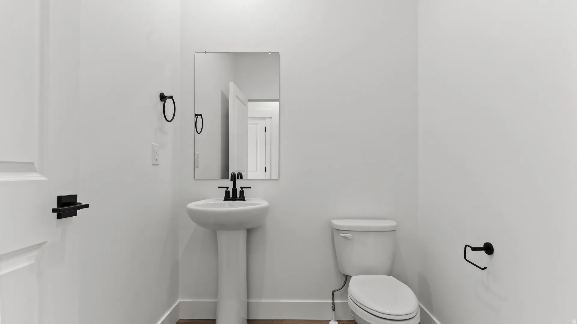 Powder room featuring a pedestal sink with matte black faucet, wall-mounted rectangular mirror, and a white toilet