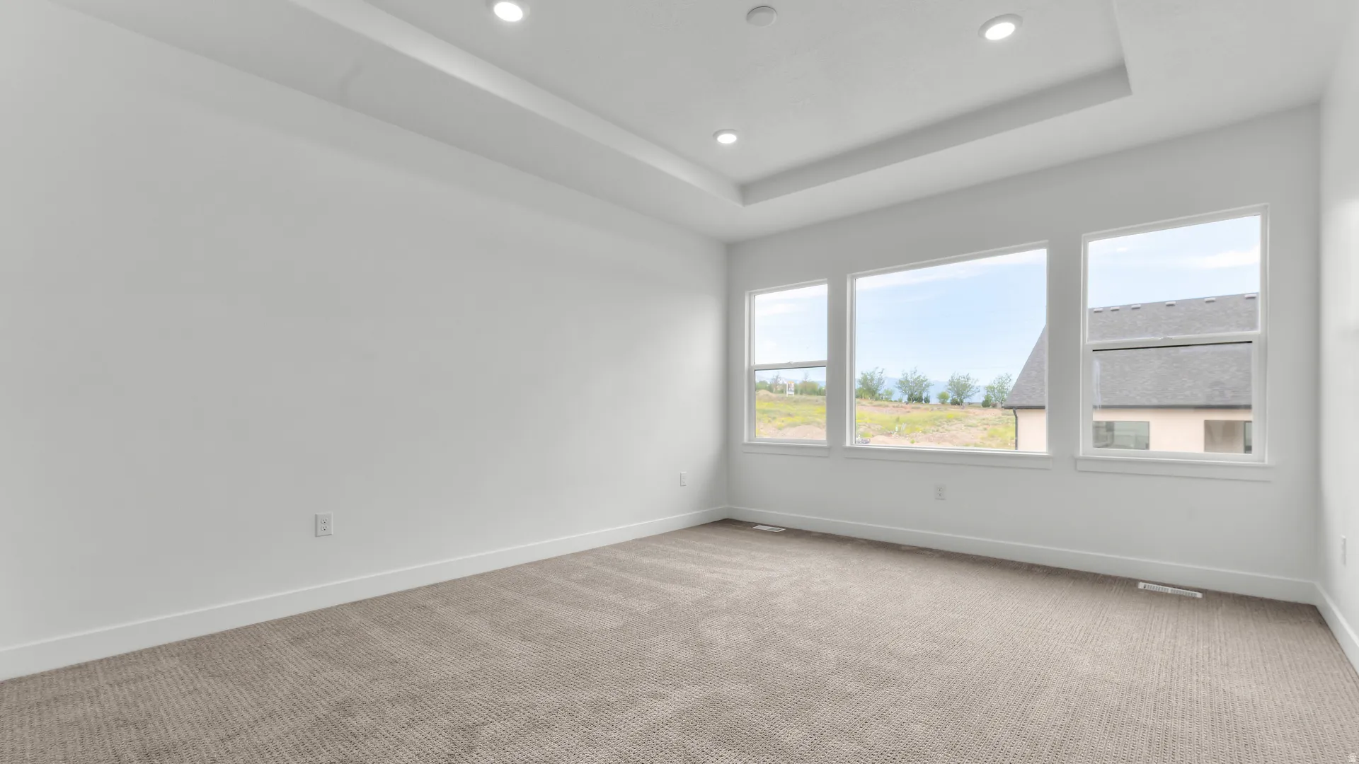 Spacious room featuring multiple windows, recessed lighting, a tray ceiling, light-toned carpet, and clean white walls