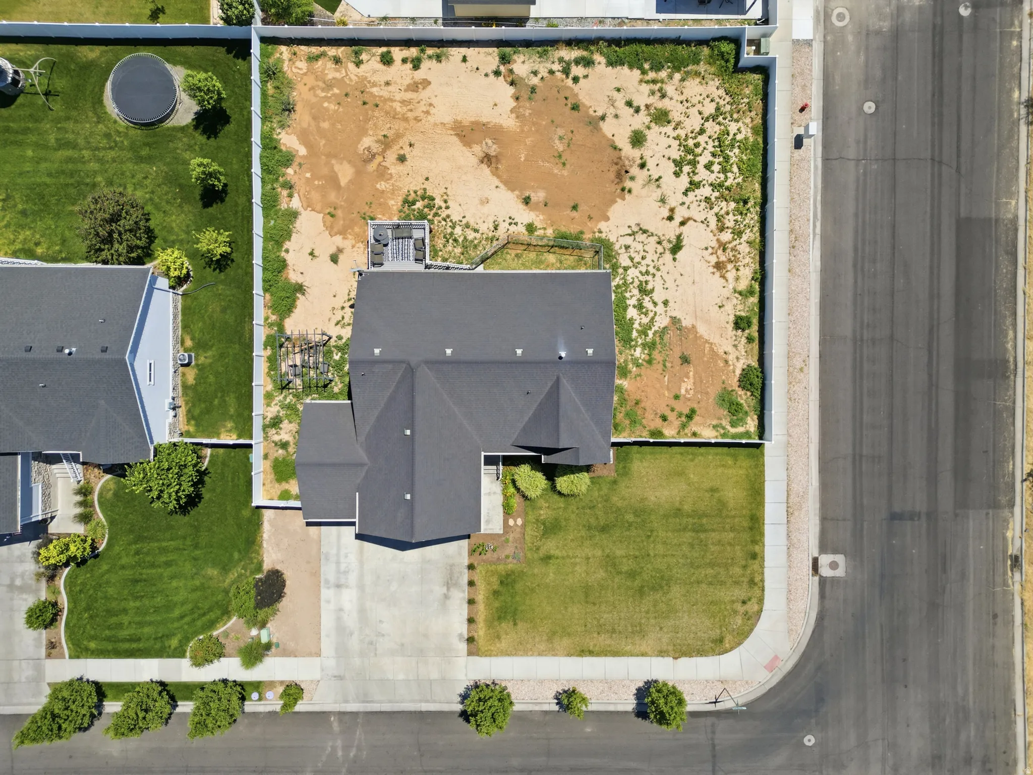 Expansive corner lot featuring a residence with a dark shingle roof, a concrete driveway, and established front yard landscaping