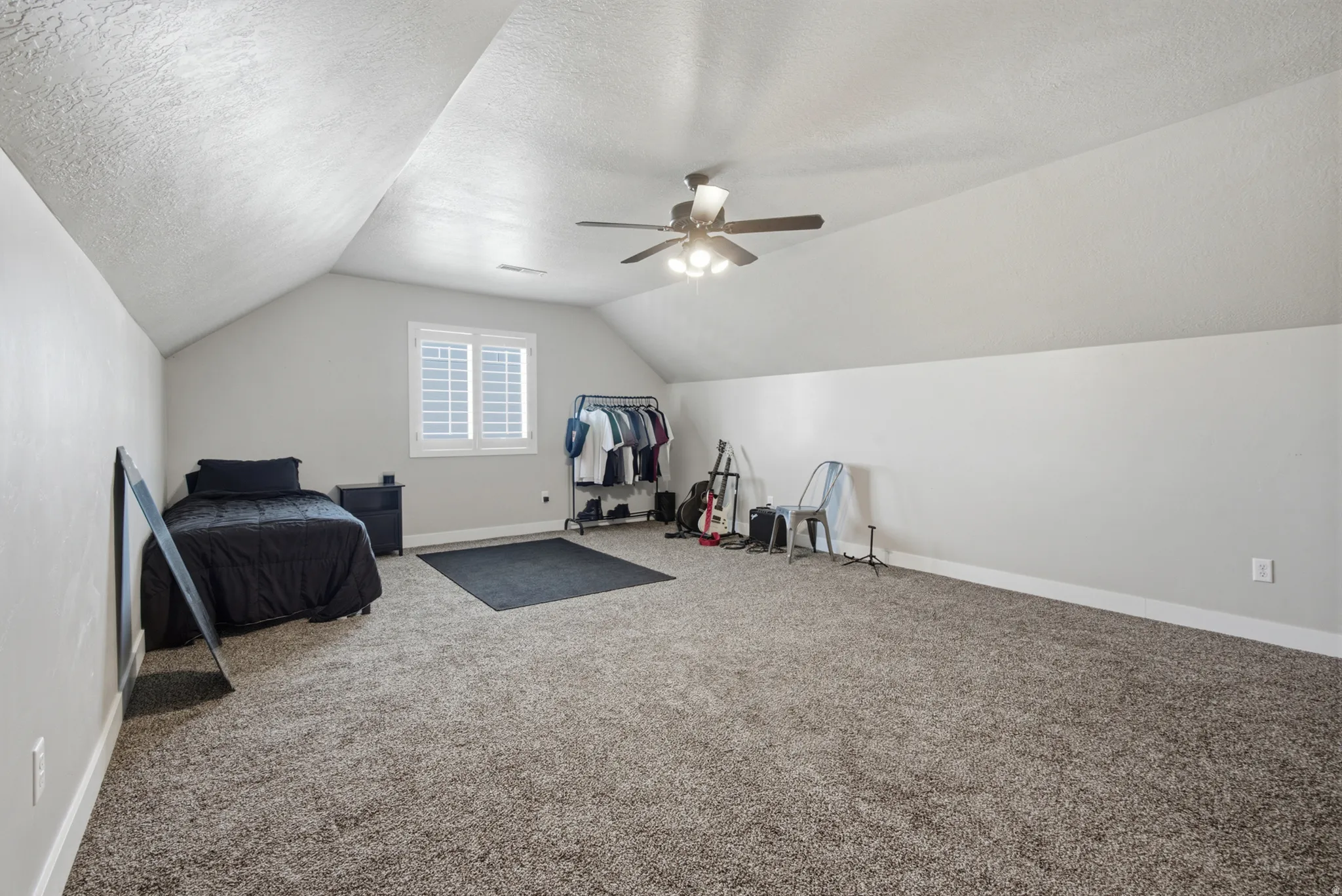 Spacious room featuring vaulted ceilings, plush carpeting, a ceiling fan with integrated lighting, and a window with plantation shutters