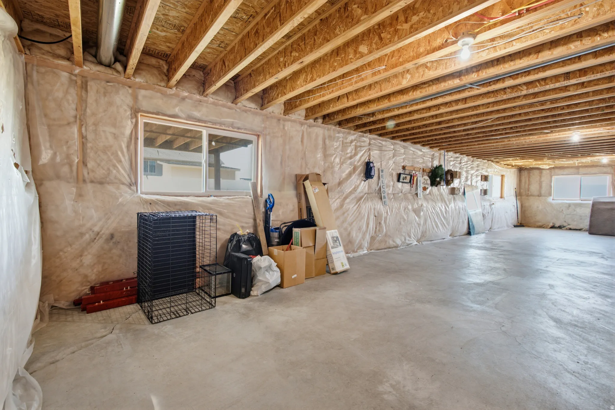 Unfinished basement featuring exposed joists, concrete flooring, two visible windows, and wall insulation