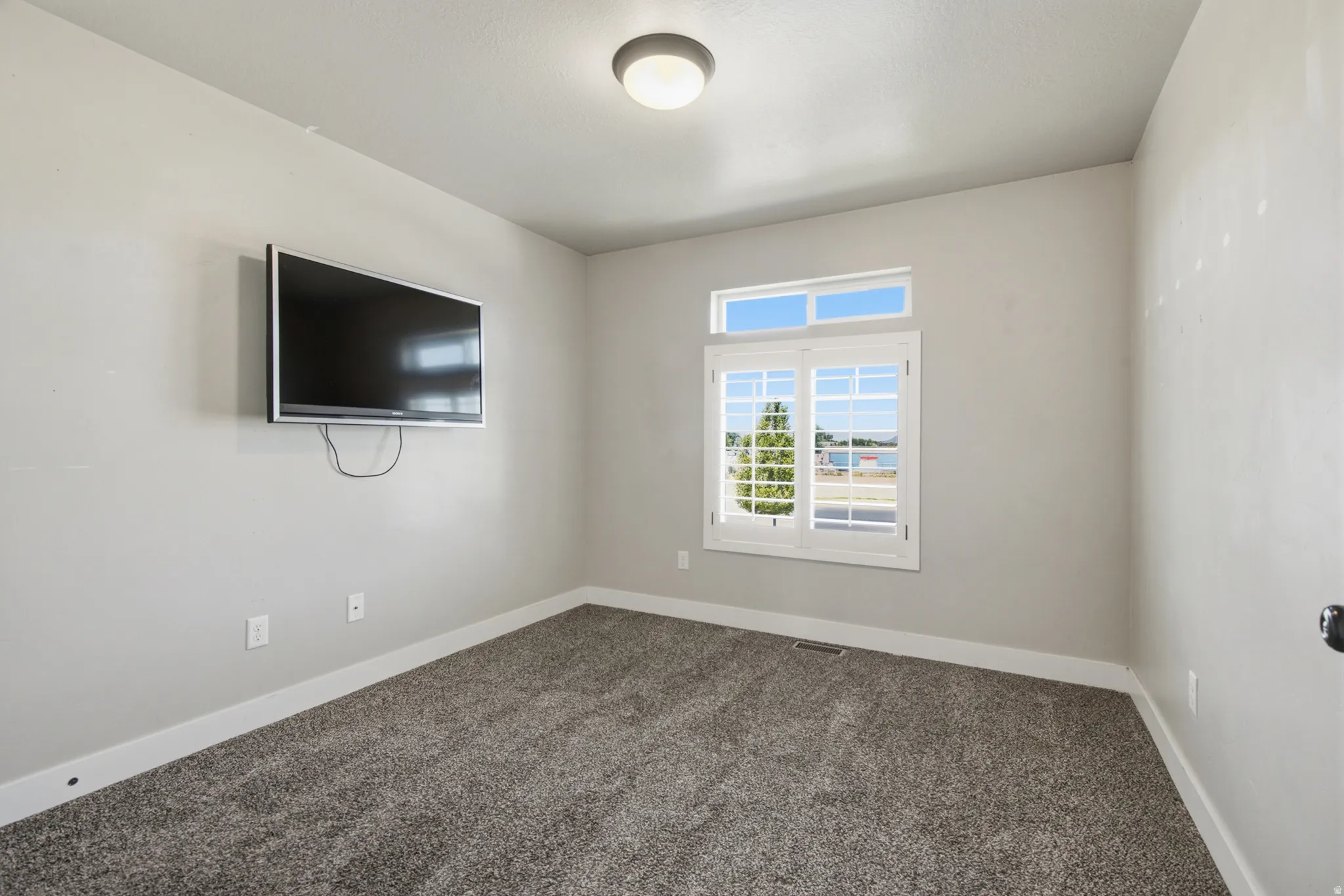 Bedroom featuring light gray wall paint, dark gray carpeting, white trim, and a white-framed window with an upper transom
