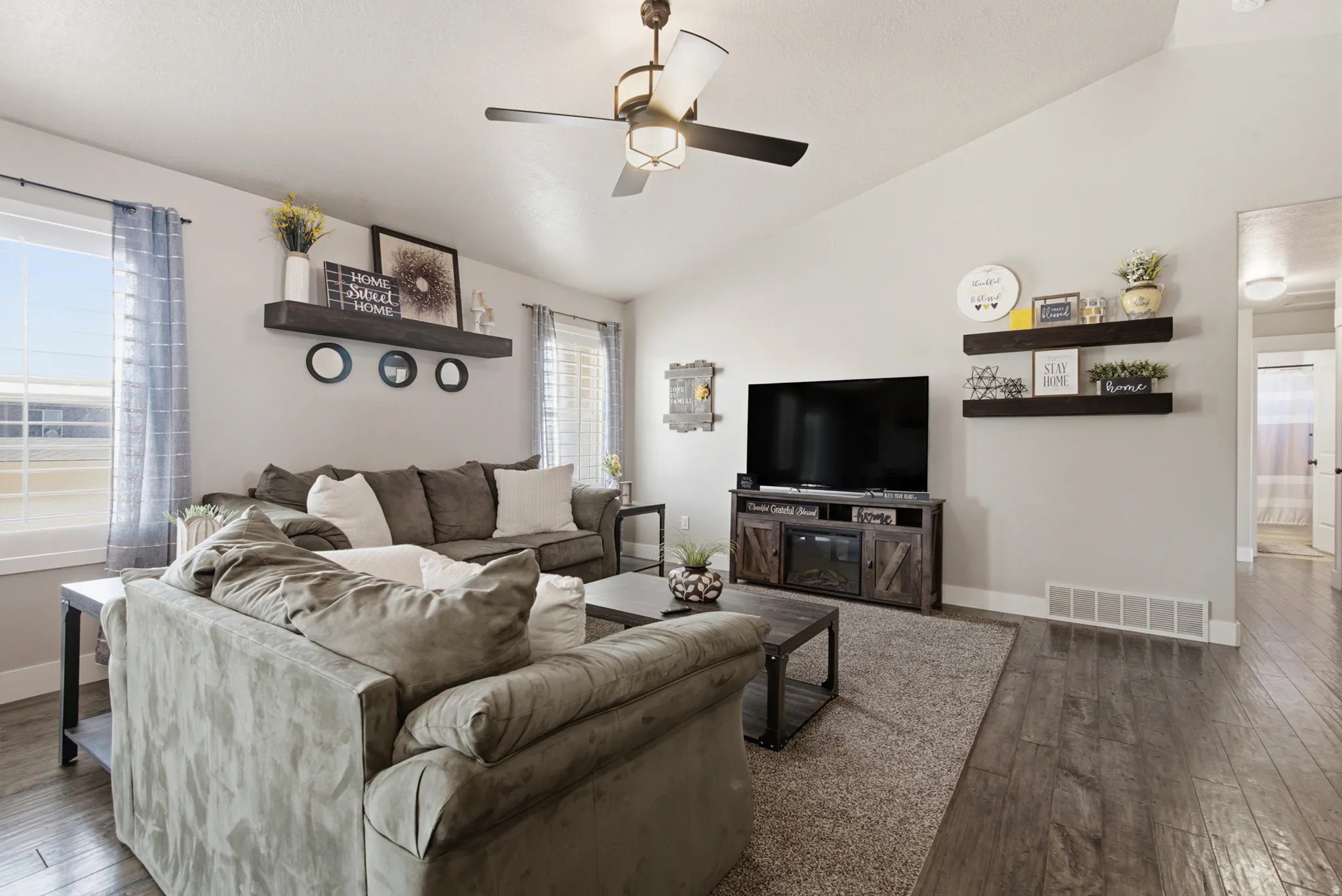 Spacious living area featuring vaulted ceilings, wood-finish flooring, and a ceiling fan with integrated lighting