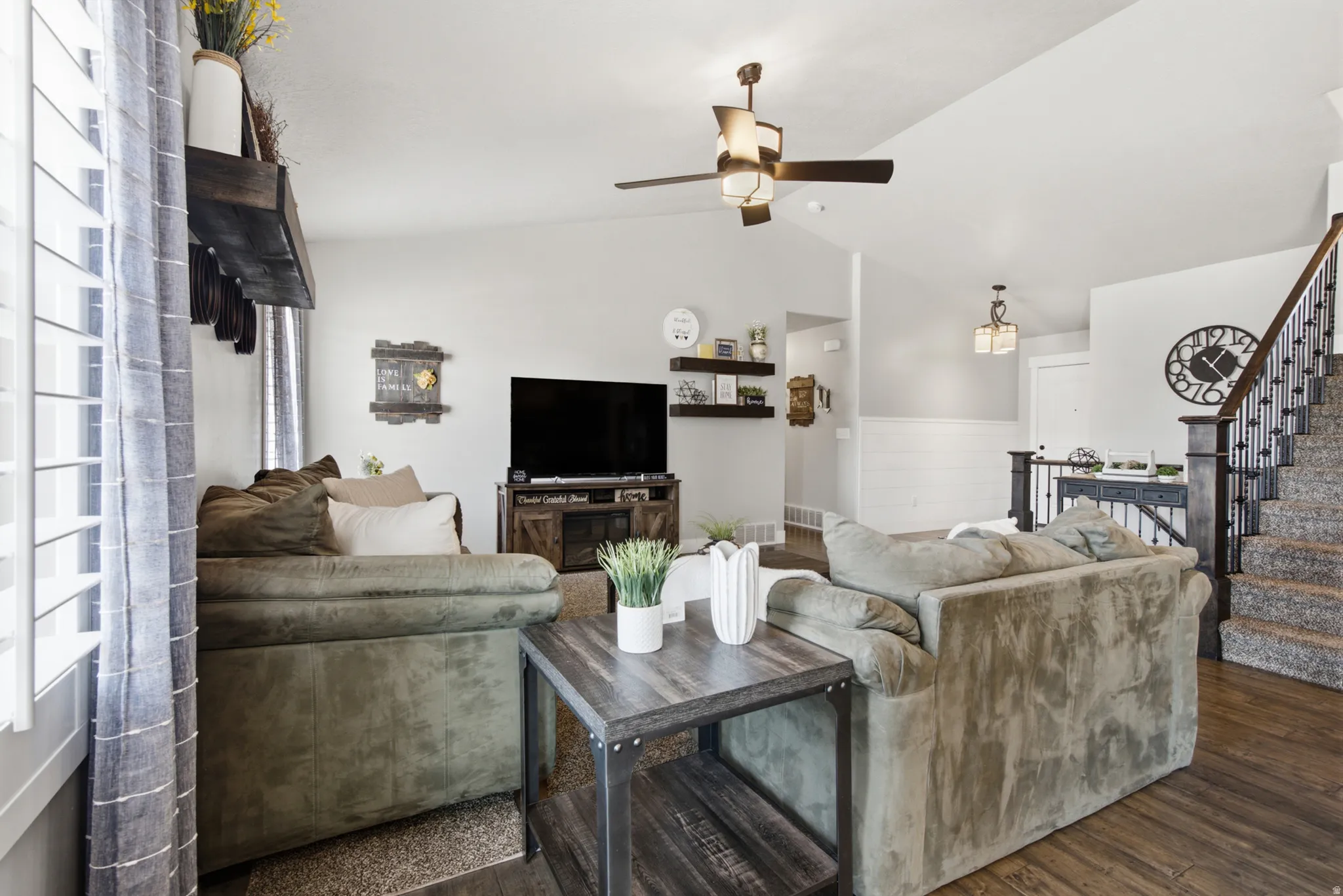 Living area featuring wood-finish flooring, a vaulted ceiling with a ceiling fan, and a staircase with dark wood newel posts and wrought iron balusters