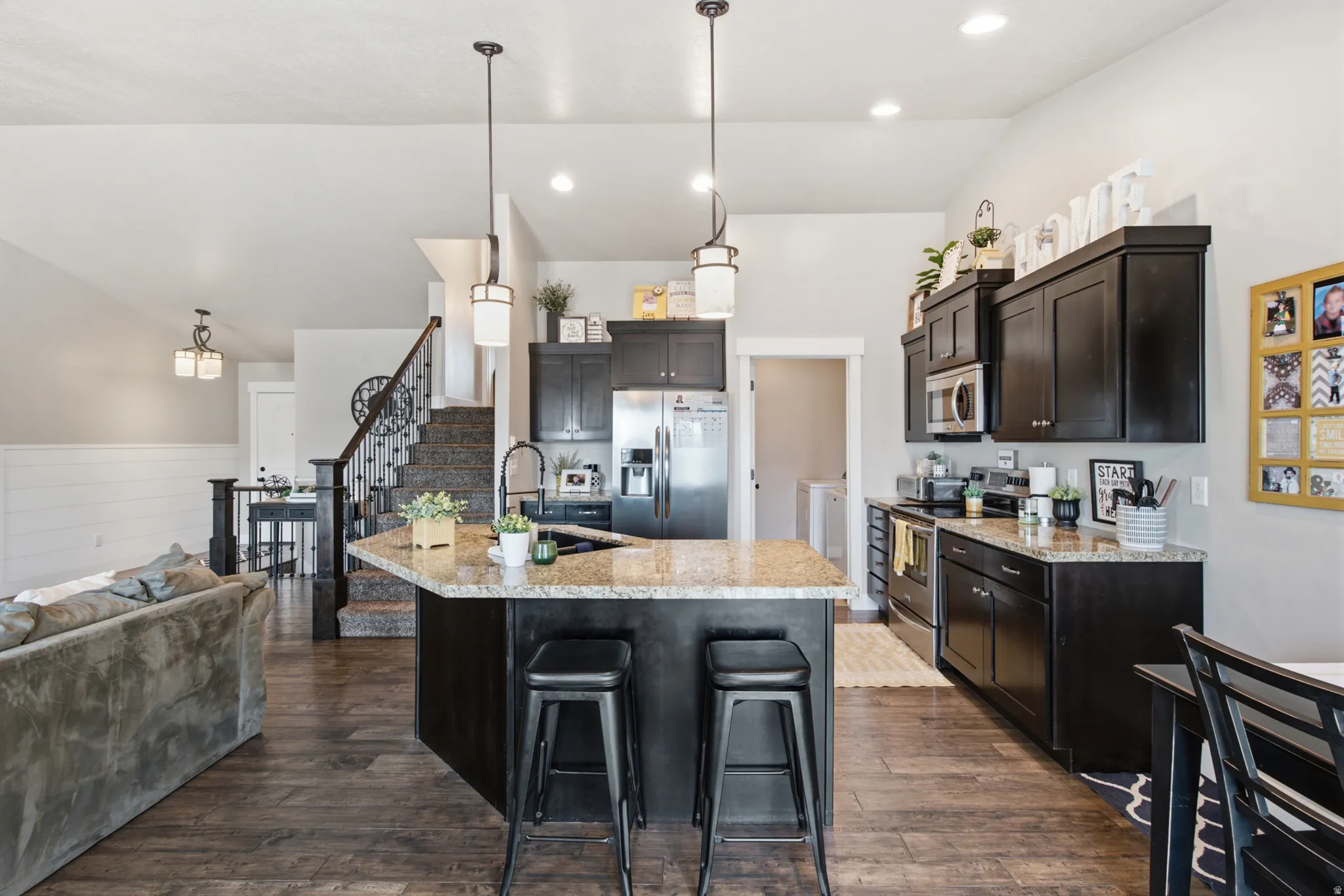 Open-concept kitchen featuring dark wood cabinetry, stainless steel appliances, a center island with bar seating, and recessed lighting