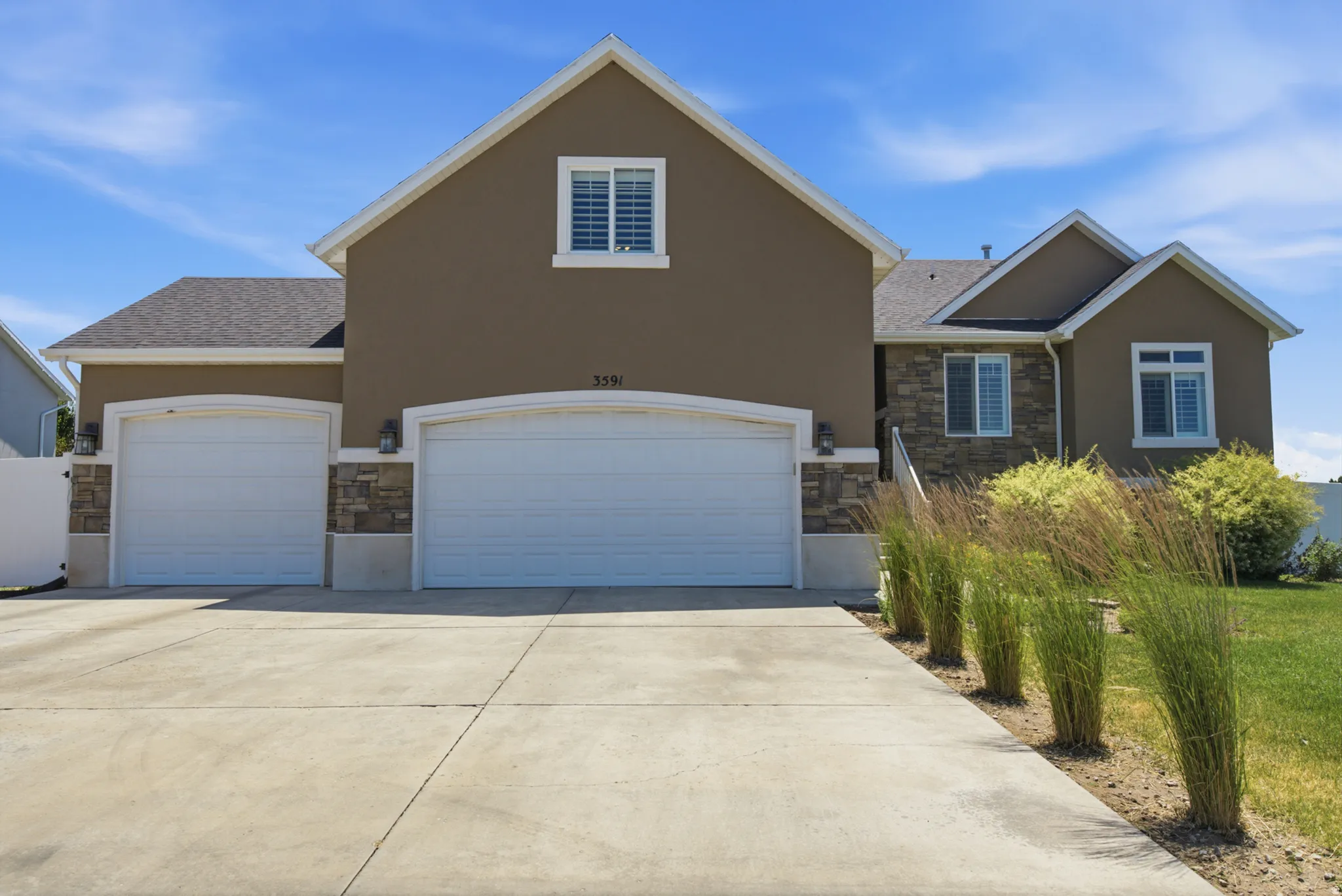 Two-car garage home featuring a stucco and stacked stone exterior, arched garage doors, and a concrete driveway