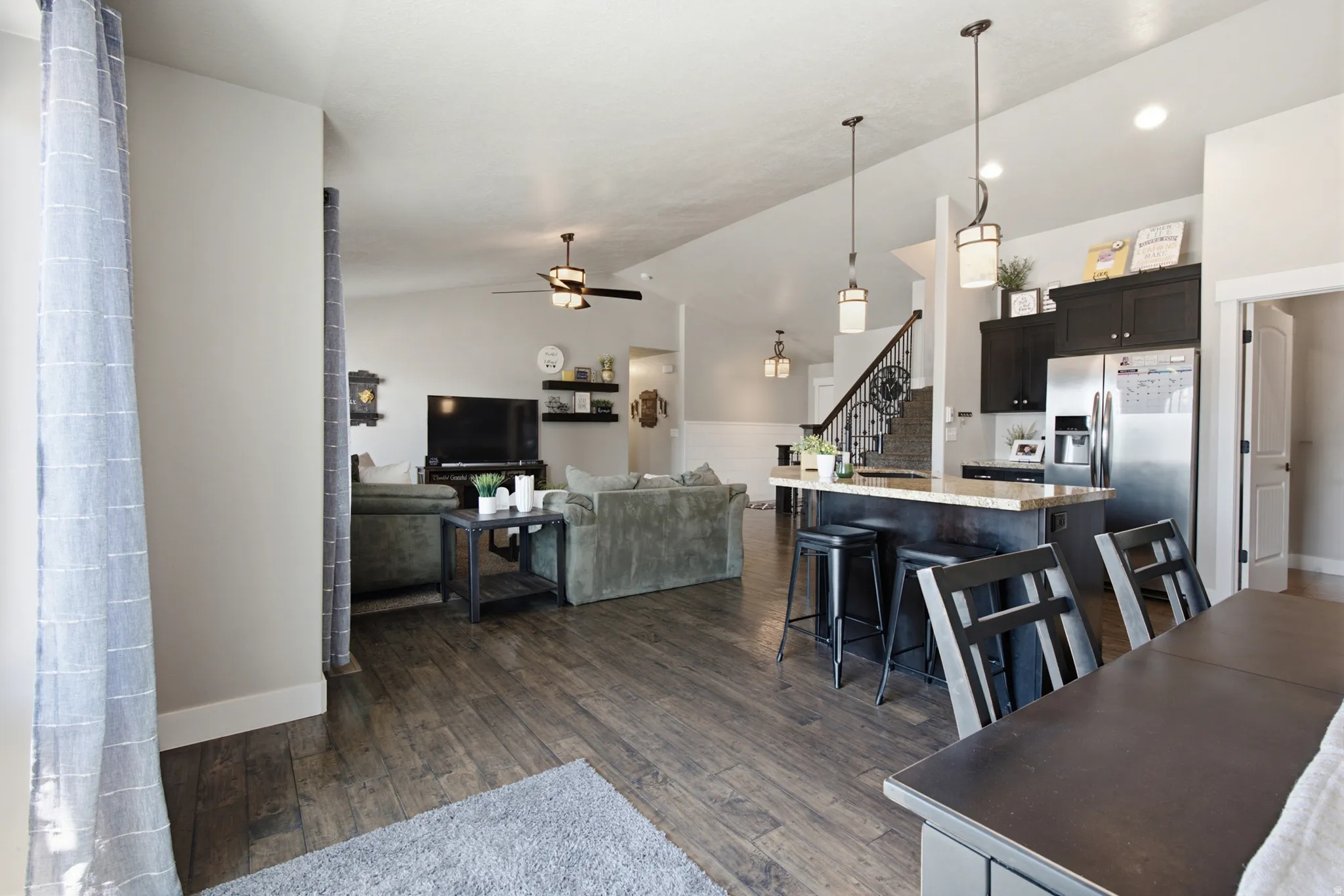 Open-concept living space featuring wood-finish flooring, a kitchen island with seating, dark wood cabinetry, stainless steel appliances, and pendant lighting